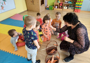 Nauczycielka wyjmuje z koszyka marchewkę i pokazuje dzieciom