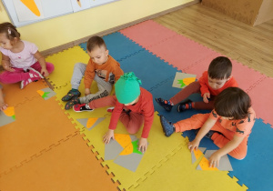 Dzieci siedzą na macie i układają rozcięty obrazek marchewki