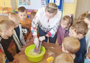 Nauczycielka ściera na tarce marchewkę, dzieci się przyglądają.