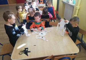 Dzieci przy stolikach robią duszki z talerzyków papierowych i bibuły
