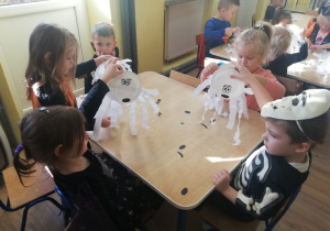 Dzieci przy stolikach robią duszki z talerzyków papierowych i bibuły