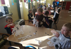 Dzieci siedzą przy stoliku i pokazują wykonane duszki