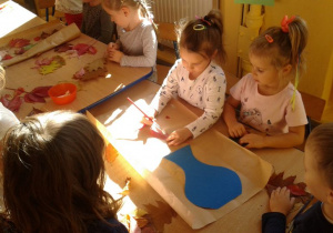Dzieci przyklejają liście na papier