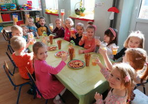 Przedszkolaki przy wspólnym stole z ciasteczkami i soczkiem