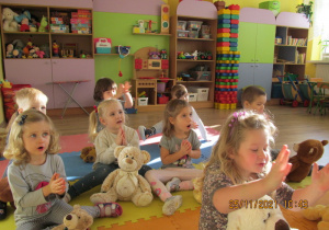 Dzieci siedzą z misiami, śpiewają i klaszczą