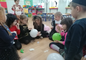 Dzieci przekuwają balony, aby poznać wróżbę zapisaną na zwiniętym pasku papieru