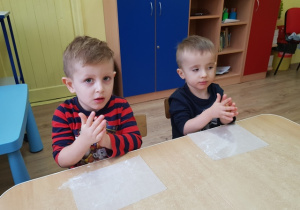 Chłopcy przygotowują pergamin posypując mąką