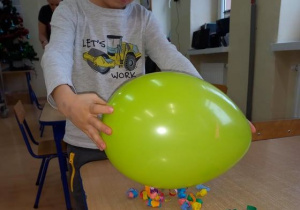 Chłopiec sprawdza czy naelektryzowany balon przyciągnie większe kawałki papieru.