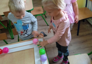 Dzieci przyklejają piłki - kropki na drewniną ramę