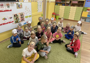 Przedszkolaki z maskami jeży siedzą na dywanie