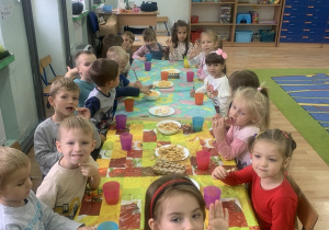 Dzieci siedzą przy stole ze słodkim poczęstunkiem