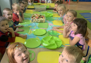Dzieci siedzą przy stole w oczekiwaniu na przygotowanie sałatki.