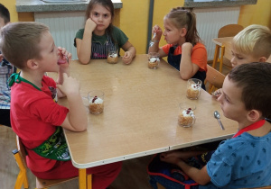 Dzieci smakują przy stolikach przygotowany deser z jabłuszkami.