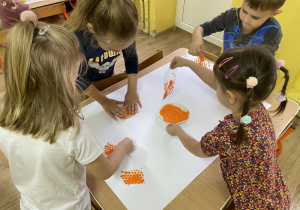 Dzieci wykonują pracę plastyczną przy stoliku.