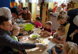 Dzieci z rodzicami wykonują sałatkę owocową