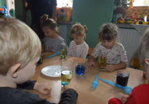 Dzieci wrzucają tabletki musujace do szklanki z oliwą i wodą.