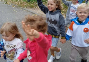 Dzieci parami przechodzą przez jezdnię podnosząc rękę do góry