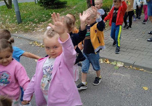 Dzieci parami przechodzą przez jezdnię podnosząc rękę do góry