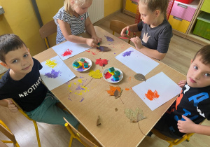 Dzieci stemplują suszonymi liśćmi, nakładając na nie farbę.