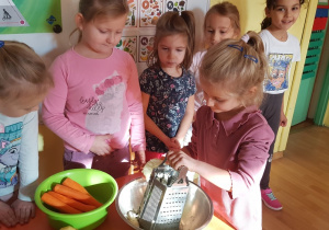 Dziewczynki ścierają jabłka na tarce.