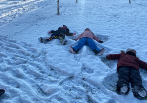 Dzieci odbijają na śniegu kształt aniołka.