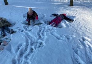 Dzieci odbijają na śniegu kształt aniołka.