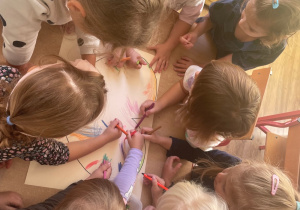 Grupa dziewczynek wspólnie koloruje narysowane na kartce papieru serce.
